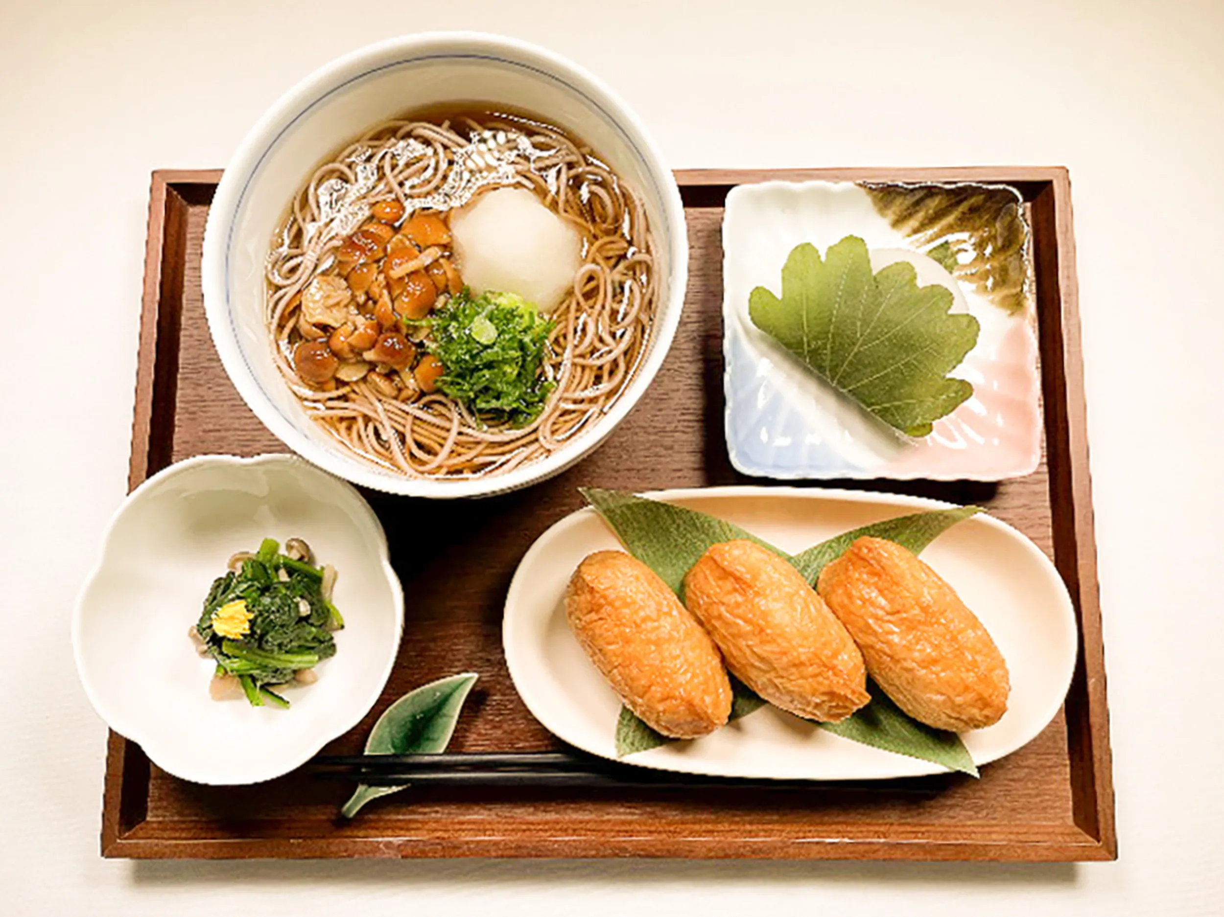 巨椋の郷で提供されるお食事膳の写真。お盆の上にそば、柏餅、小鉢、いなり寿司が乗っている。
